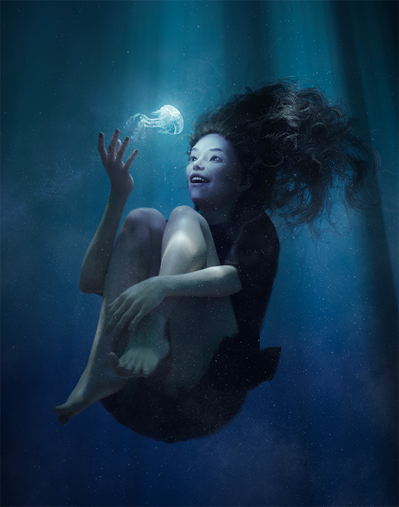 Nona floats underwater, delighted at a glowing jellyfish